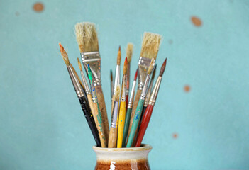 Fototapeta premium A ceramic cup with paintbrushes in various colors placed against a light blue wall