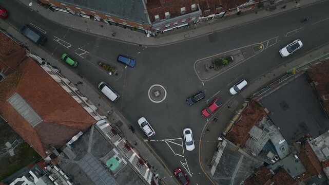 A busy intersection with cars driving through a roundabout and side streets, framed by buildings.