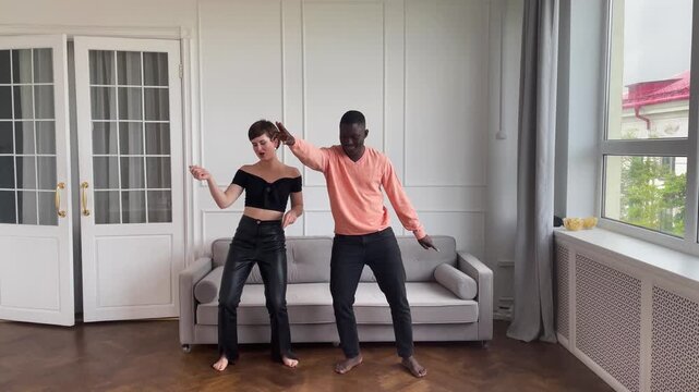 Couple of young african american man and caucasian woman dancing at home