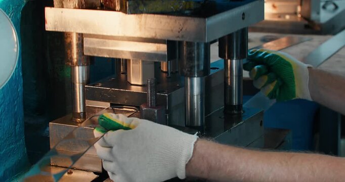 Blue collar worker operating metal stamping press in factory workshop. Industrial production and manufacturing labor