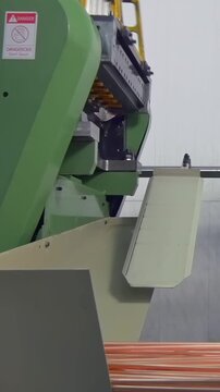 Industrial machinery orchestrates the feeding of copper rods, guiding each one into a precise processing sequence. This continuous action unfolds within a bustling daytime factory environment.