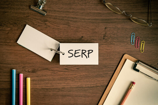 Eye-catching image of SERP text on word card. The word stands for Search Engine Result Page. Shown with pens, clipboard, glasses.