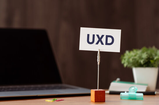 Eye-catching image of UXD text on card. The word stands for User eXperience Design. Shown with laptop, clips.