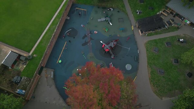 An aerial view shows a vibrant playground with a ship-like play structure, swings, slides, and a net. A caf&eacute; and green spaces are also visible.