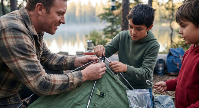 Father and sons setting up tent near lake