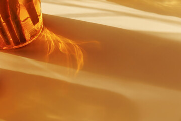 Abstract golden light refraction and elongated shadow from amber glass in warm sunlight creating...