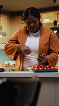 Black content creator cutting avocado in food video at the counter, influencer recording healthy breakfast idea indoors. Woman vlogger explaining meal prep and culinary recipe development.