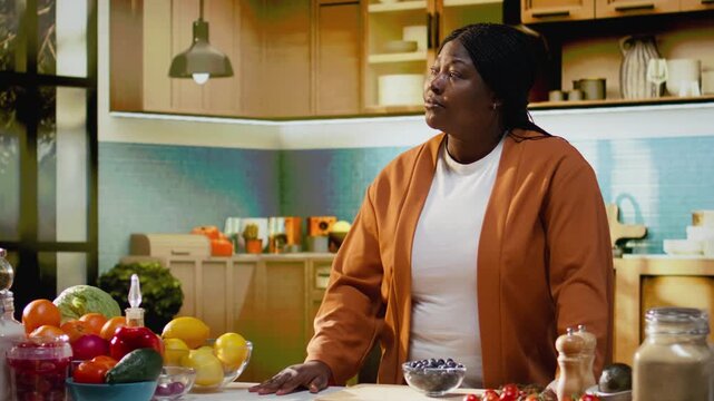Portrait of african american woman smiling and filming online tutorial in home kitchen studio, creating gourmet dish with fresh ingredients and cooking process. Content creator home chef.