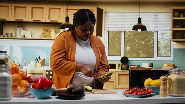 Cutting avocado, cooking video, recipe preparation on toast, black woman, food vlogger working at the counter. Influencer explaining culinary tutorial and meal prep, nutritious healthy choice.