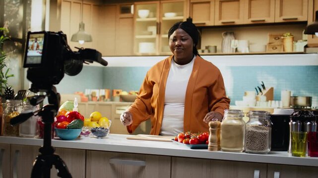Tripod and camera, African american, food vlogger, culinary content, recording behind the scenes in home studio kitchen. Woman influencer ensuring meal preparation for online audience.