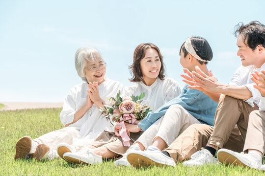 A family sitting on a park/hill with a view of the blue sky; a parent-child family; a three-generation family (father, mother, daughter, grandmother, grandfather).