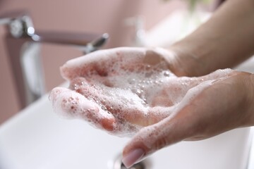 Fototapeta premium Woman washing hands with soap near white sink indoors, closeup