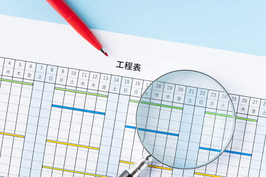 工程表と虫眼鏡と赤いペン
