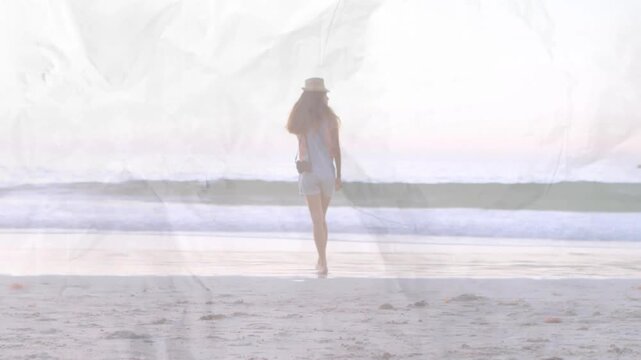 Adult woman walking from sand to shore, holding camera, crumpled overlay framing horizon for travel
