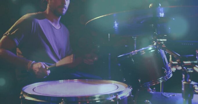 Drummer raising hand, adjusting kit, playing snare and toms, starting music set under teal lights