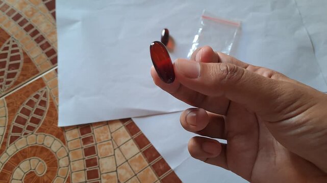 Close-up of Asian male hands demonstrating the dangers of illegal drugs using capsules and a small plastic bag of white powder as visual aids for drug abuse prevention education.