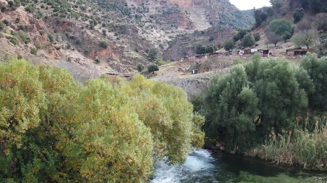 Mountain river flowing through green vegetation and rocky hills in the Oum Er-Rbia valley of the Middle Atlas near Khenifra, Morocco.