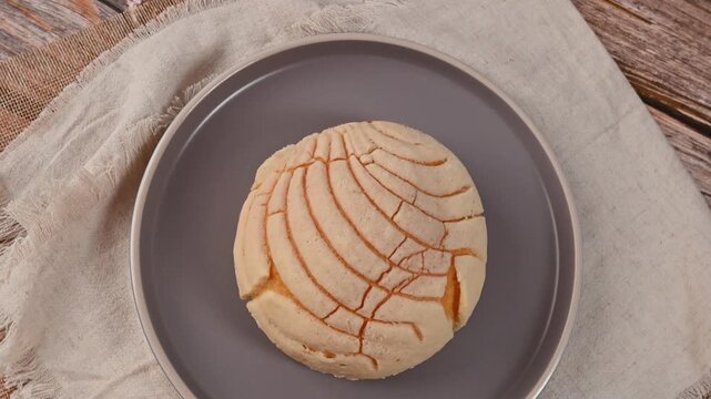 Traditional vanilla concha Mexican sweet bread on a gray plate with rustic wooden background, camera rotates
