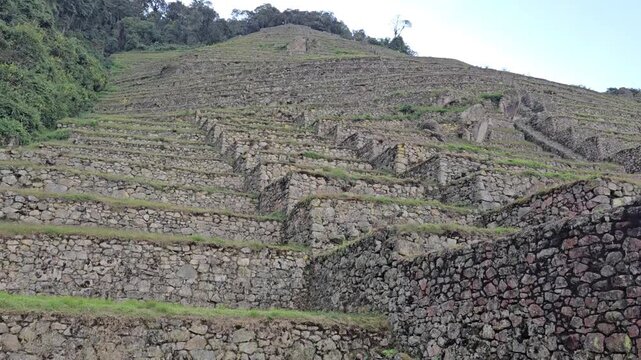 Intipata, Peru - 26 June 2024. Stone terraces ascend a green mountainside, with layered walls and pathways forming stepped agricultural levels.
