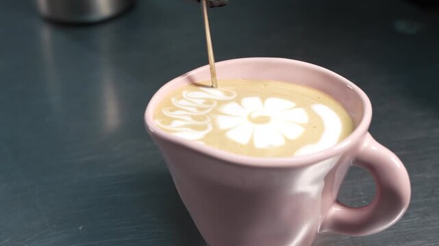 Close-up of a barista refining latte art by adding detailed side patterns around a central flower design in coffee. Milk foam decoration and professional beverage styling.