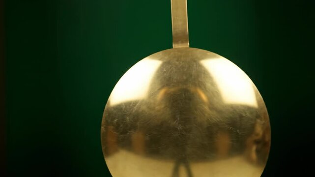 The pendulum of an old grandfather clock swinging slowly and rhythmically, isolated on solid green background pendulum of an old, passing time, night