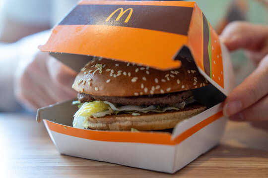 Belgrade, Serbia: July 3, 2024: Hands opening a McDonalds burger box to reveal a sesame bun hamburger with patty and shredded lettuce, fast food takeaway close up on a table