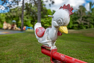 Old metal rocking chicken, animal form, riding playground equipment for young children at a park, school, with chipped white and red paint. 