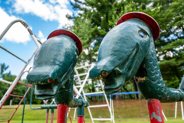 Close up of old metal climbing playground equipment with strange green dinosaur heads and red hats for young children at a park, school. 