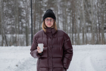 caucasian woman standing with cup, maroon puffer and beanie, glasses on, direct gaze, neutral snowy background, confident streetwear posture, fashionforward winter mood, influencer energy © Alexander