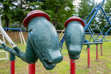 Close up of old metal climbing playground equipment with strange green dinosaur heads and red hats for young children at a park, school. 