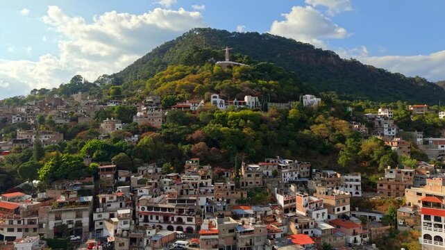 Bird's-eye view of residential houses surrounding the green hillside of Atachi with the Monumental Christ of Taxco in the evening light, Mexico