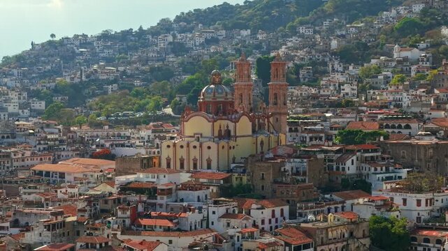 Telephoto establishing aerial view of the Santa Prisca temple in the city of Taxco de Alarcon, Guerrero, Mexico. White houses with tiled roofs on a sunny day, high frame rate.