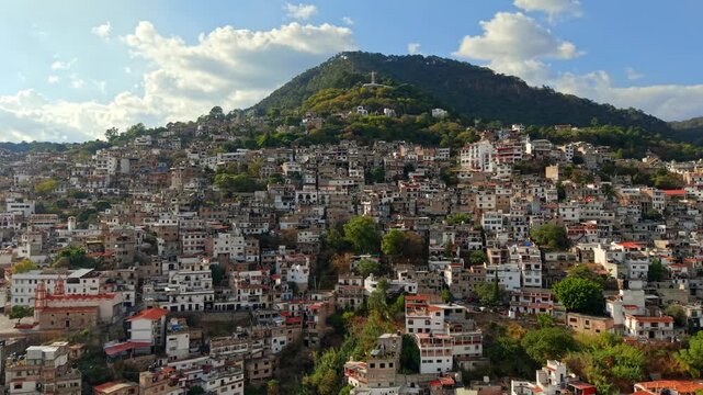 Panoramic aerial view dolly in of the houses on the slopes of Atachi Hill with the monumental Christ statue in Taxco, Guerrero, Mexico