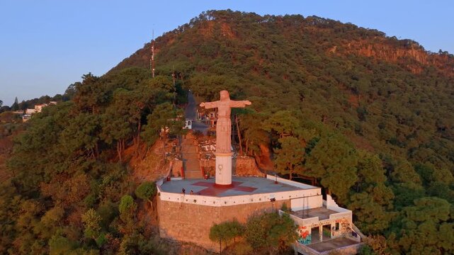 Aerial view dolly in of the Monument to Christ the King in Taxco on the orange-colored Atachi hill at sunset, Guerrero, Mexico