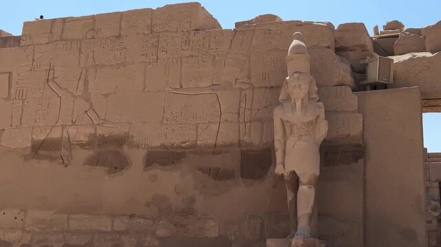 A static shot of an ancient Egyptian pharaoh statue wearing the double crown next to stone wall reliefs in the Karnak Temple complex, Luxor