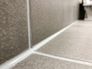 Fototapeta premium Close-up view of newly installed grey tiles on a bathroom wall and floor, featuring neat white grout lines and sealant in the corner.