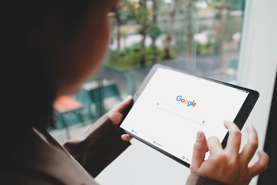 Bangkok, Thailand. MAR 24, 2026; Over the shoulder view of a person using a tablet to browse the Google search engine homepage while sitting near a bright window.