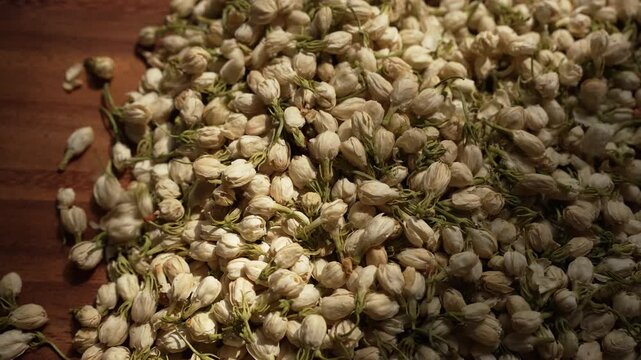 Cinematic top view of dried jasmine buds falling onto rustic wooden floor, showcasing delicate patterns, organic textures, and soft natural daylight.