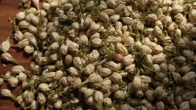 Cinematic top view slow zoom out revealing dried jasmine buds falling onto rustic wooden floor, showcasing composition, natural light, and organic textures.