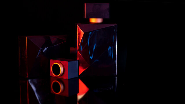 Luxury perfume bottles with neon red and blue lighting on black background copy space Elegant luxury perfume bottles illuminated with dramatic red and blue neon lighting on a black reflective surface.