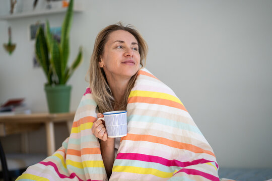 Happy optimistic woman drinking coffee in cozy bed in early morning, lady awakening in good mood shows positive uplifted expression, happy healthy female enjoys beverage and peaceful comfy home life.