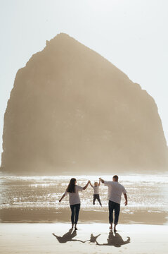 The photograph depicts a family walking along the seashore. The man and woman are holding hands with a small child, who walks between them. They head toward the sea, enjoying the walk 