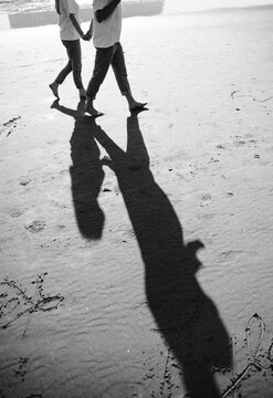 The photograph shows a small child standing on a sandy beach, looking toward adults holding hands in the foreground. The child appears joyful and confident, the center of attention. Warm sunlight illu
