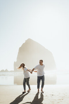 The photograph shows a man and woman dancing on a sandy beach, holding hands. They are smiling and appear happy, enjoying their time together. Their movements are light and natural, creating a sense o