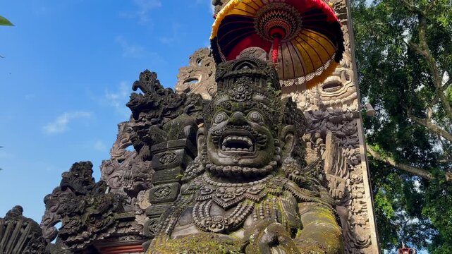 Traditional Balinese stone guardian statues at Hindu temple entrance in Bali, Indonesia. Sacred architecture with symbolic carvings and parasols. Concepts of religon, culture, and travel. 