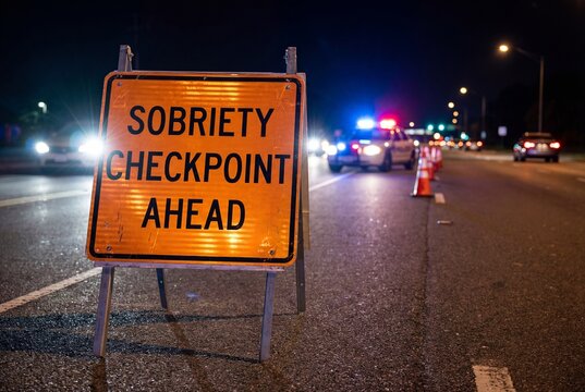 Sobriety checkpoint sign on a road at night with police car lights