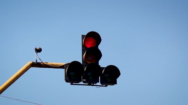 Traffic signal changing from red to green with amber transition against blue sky, symbol of start, movement, road safety control and urban traffic management system.