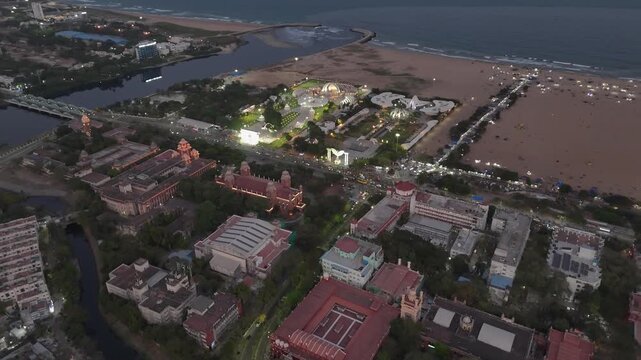Drone shot capturing the glowing Anna and MGR Memorial complexes near Marina Beach, Chennai, with vibrant city traffic, beach activity, and stunning coastal scenery at twilight.