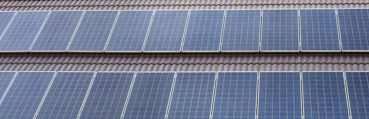 Fototapeta premium Solar panels installed on a dark tiled roof of a house