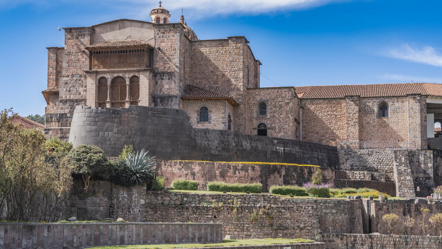 The ancient Inca Temple of the Sun Coricancha. Masonry  walls, parabolic enclosure wall, columns, arches, narrow windows. Green plants on the terraces. Blue sky, clouds. Peru. Cusco.
 